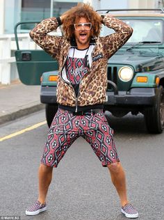 a man with an afro standing on the street in front of a jeep and holding his hands behind his head