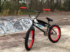 a black bike with red rims parked in front of a graffiti - covered wall