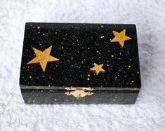 a black box with gold stars on the lid and bottom, sitting on a white surface