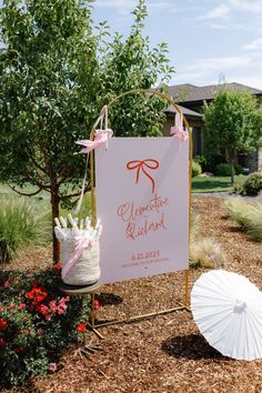 a white umbrella sitting next to a sign on top of a dirt field with flowers