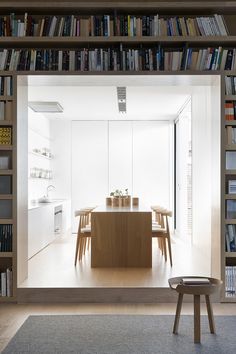 a dining room table surrounded by bookshelves in front of a kitchen