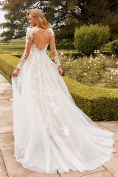 a woman in a white wedding dress standing on a stone walkway with her back to the camera