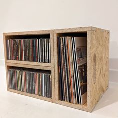 a wooden box with several different types of records in it on a white surface next to a wall