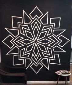 a large black and white snowflake on the wall next to a small stool