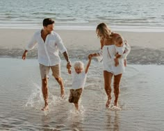 a man, woman and two children are walking in the water at the beach together