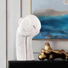 a white sculpture sitting on top of a black table next to a painting and two gold sculptures