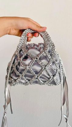 a hand holding a silver purse on top of a white wall