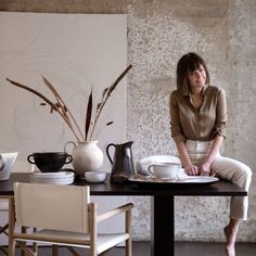 a woman sitting at a table with coffee cups and saucers in front of her