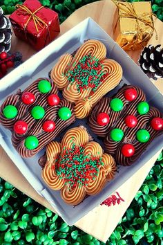 a box filled with lots of decorated cookies on top of a green table covered in pine cones