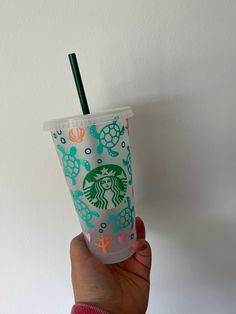 a hand holding a starbucks cup with a green lid and straw in front of a white wall