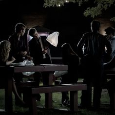 a group of people sitting at a picnic table in the dark with an umbrella over their heads