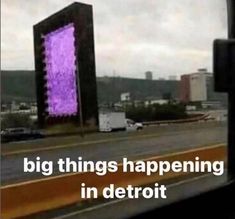 a big building sitting on the side of a road next to a street sign that says, big things happening in detroit