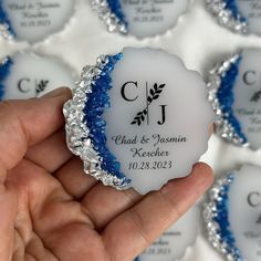 a hand holding a small white and blue wedding ornament in front of rows of smaller ones