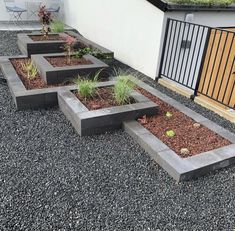 several concrete planters are lined up in the gravel near a building with a gate