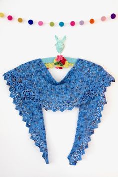 a blue shawl hanging from a string on a white wall with multicolored beads