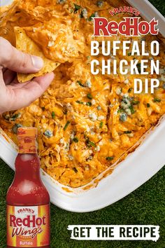 a hand holding a tortilla chip over a casserole dish with red hot buffalo chicken dip