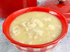 a red and white bowl filled with soup next to a red pot on the table