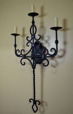 an iron wall mounted candle holder with three candles on the top and one light in the middle