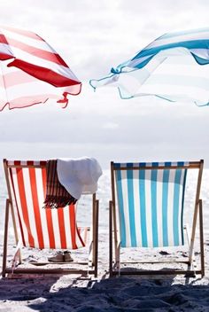 two beach chairs sitting on top of a sandy beach