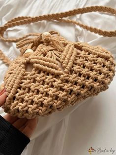 a hand holding a crocheted purse on top of a bed