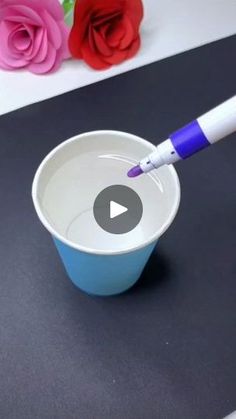 a white and blue cup with a purple pen in it next to some pink roses