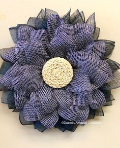 a blue and white mesh flower with a woven button on the center is hanging from a wall