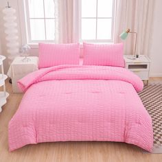 a bed with pink bedspread and pillows in a room next to a window