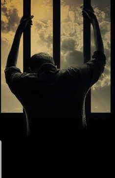 a man is standing behind bars with his hands in the air and looking at the sky