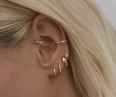 a woman with blonde hair wearing three gold ear cuffs and an earring that is shaped like a leaf