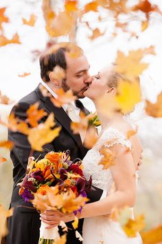 a bride and groom kissing in the fall leaves