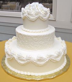 a three tiered white wedding cake sitting on top of a yellow tablecloth covered table