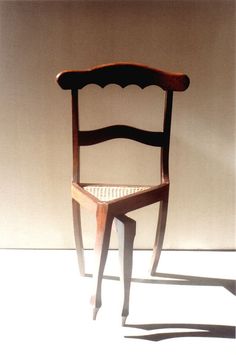 a wooden chair sitting on top of a white floor next to a wall with a shadow cast on it