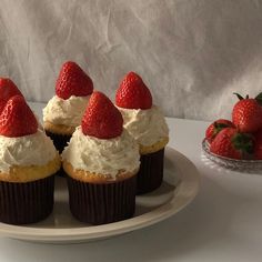 several cupcakes with strawberries on top sit on a plate