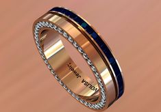 a wedding band with blue and gold inlays is shown on a pink background