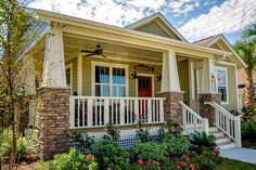 the front porch of a house with white railings and red door, surrounded by flowers