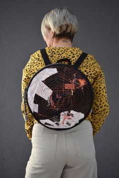 a woman with grey hair wearing a yellow shirt and white pants is holding a black backpack