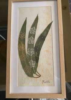 a painting of three green leaves with white flowers on them in a wooden framed frame