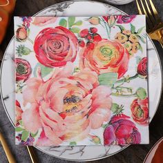 a white plate topped with a napkin covered in red and orange flowers on top of a marble table