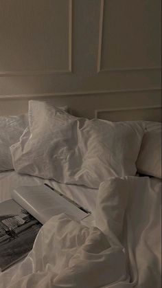 an open book sitting on top of a bed covered in white sheets and pillows,