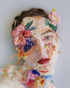 a woman with flowers painted on her face and body is wearing pearls, beads and butterflies