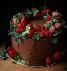 a chocolate cake topped with strawberries and green leaves on top of a wooden table