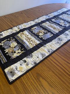 a quilted table runner on top of a wooden table covered in black and white flowers