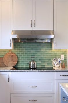 a white kitchen with green tile backsplash and stainless steel range hood over the stove