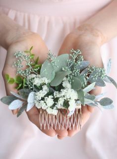 a person holding a flower and comb in their hands with greenery on the top