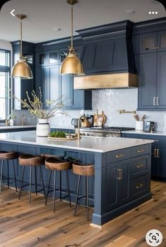 a large kitchen with blue cabinets and gold pendant lights hanging from the ceiling, along with bar stools