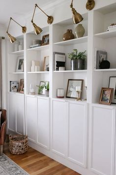 a living room filled with lots of white bookshelves covered in gold lighting fixtures