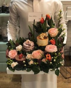 a man is holding a bouquet of flowers and cakes in front of his face while wearing a white shirt