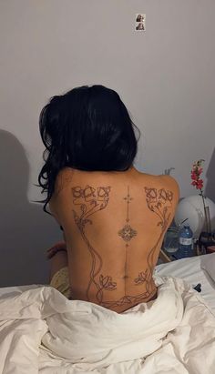 a woman with tattoos on her back sitting in bed