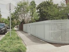 a car parked next to a white fence on the side of a road in front of a house