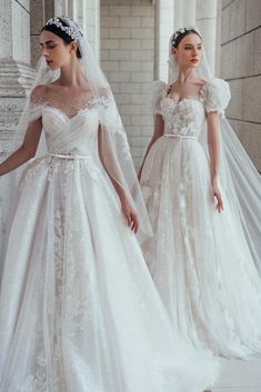 two brides in wedding gowns with veils on their heads, one wearing a white dress